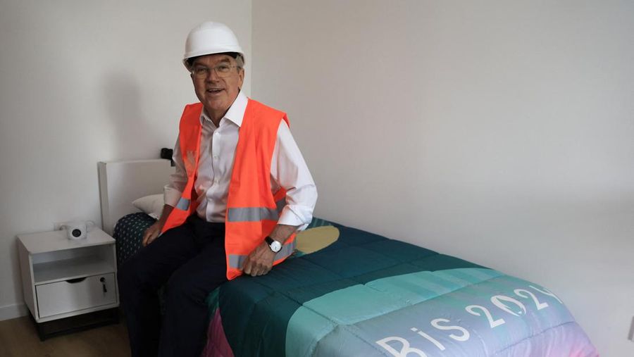 International Olympic Committee (IOC) president Thomas Bach sits on a bed as he visits the Athletes' village in Saint-Ouen-sur-Seine, outside Paris, Tuesday, July 25, 2023. (Pascal Rossignol/Pool via AP)