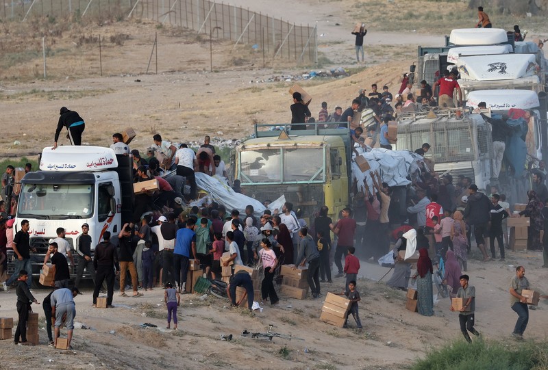 Warga Palestina menaiki truk untuk mengambil bantuan yang dikirim ke Gaza melalui dermaga buatan AS, di tengah konflik yang sedang berlangsung antara Israel dan kelompok Islam Palestina Hamas, terlihat dari pusat Jalur Gaza, 18 Mei 2024. (REUTERS/Ramadan Abed)