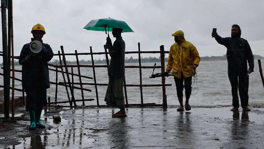 Orang-orang berdiri di tepi sungai Kholpetua sementara seorang sukarelawan memperingatkan orang-orang menggunakan megafon sebelum Topan Remal melanda negara itu di daerah Shyamnagar di Satkhira, Bangladesh, 26 Mei 2024. (REUTERS/Mohammad Ponir Hossain)