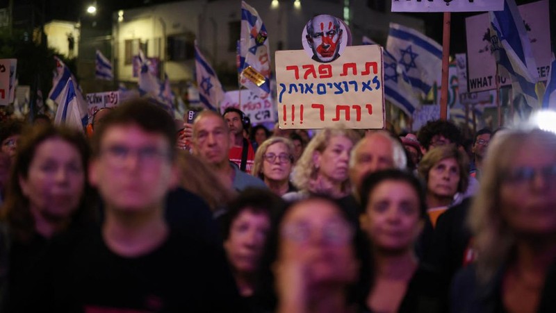 Seorang pengunjuk rasa menyalakan suar ketika mereka berdiri di dekat api yang menyala selama protes terhadap pemerintahan Perdana Menteri Israel Benjamin Netanyahu dan menyerukan pembebasan sandera yang diculik dalam serangan mematikan terhadap Israel pada 7 Oktober oleh kelompok Islam Palestina Hamas, di Tel Aviv , Israel, 25 Mei 2024. (REUTERS/Marko Djurica)