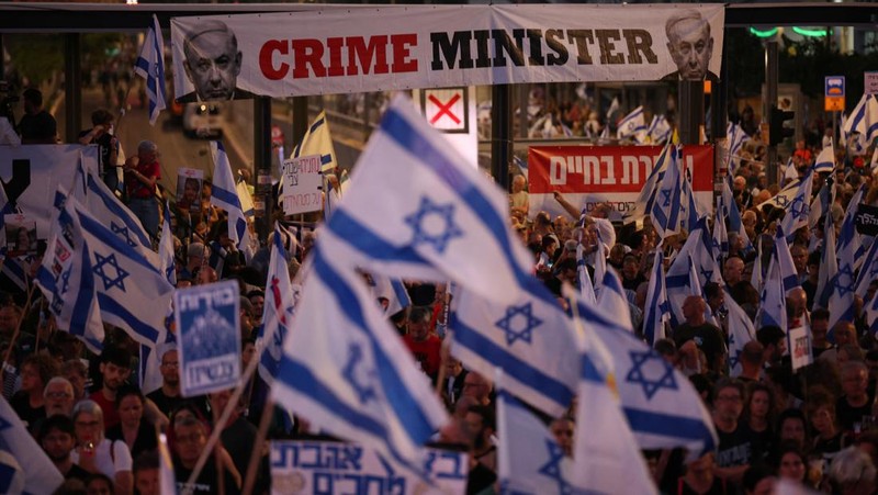 Seorang pengunjuk rasa menyalakan suar ketika mereka berdiri di dekat api yang menyala selama protes terhadap pemerintahan Perdana Menteri Israel Benjamin Netanyahu dan menyerukan pembebasan sandera yang diculik dalam serangan mematikan terhadap Israel pada 7 Oktober oleh kelompok Islam Palestina Hamas, di Tel Aviv , Israel, 25 Mei 2024. (REUTERS/Marko Djurica)