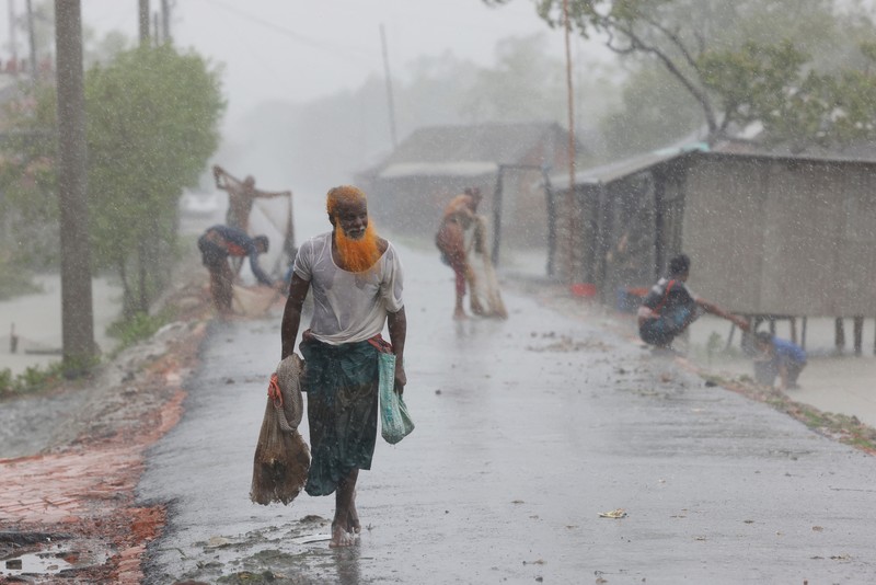 Seorang pria menyelamatkan gerobak dan material lainnya saat air mengalir ke pantai Kuakata di pesisir Teluk Benggala akibat mendekatnya Topan Remal di Barisal, Bangladesh, Minggu, 26 Mei 2024. (AP Photo/Abdul Goni)
