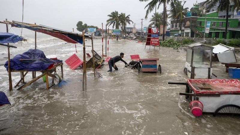 Seorang pria menyelamatkan gerobak dan material lainnya saat air mengalir ke pantai Kuakata di pesisir Teluk Benggala akibat mendekatnya Topan Remal di Barisal, Bangladesh, Minggu, 26 Mei 2024. (AP Photo/Abdul Goni)