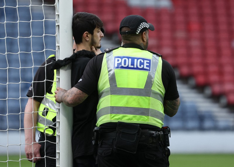 Polisi menahan seorang pengunjuk rasa yang diikat ke tiang gawang di Hampden Park, Glasgow, Skotlandia, Jumat (31/5/2024). (REUTERS/Russell Cheyne)