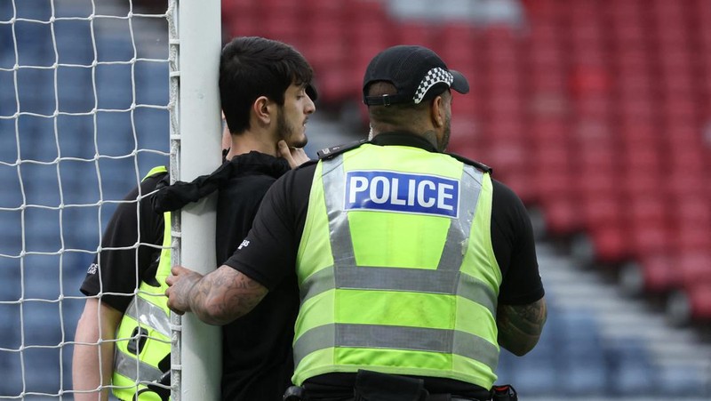Polisi menahan seorang pengunjuk rasa yang diikat ke tiang gawang di Hampden Park, Glasgow, Skotlandia, Jumat (31/5/2024). (REUTERS/Russell Cheyne)