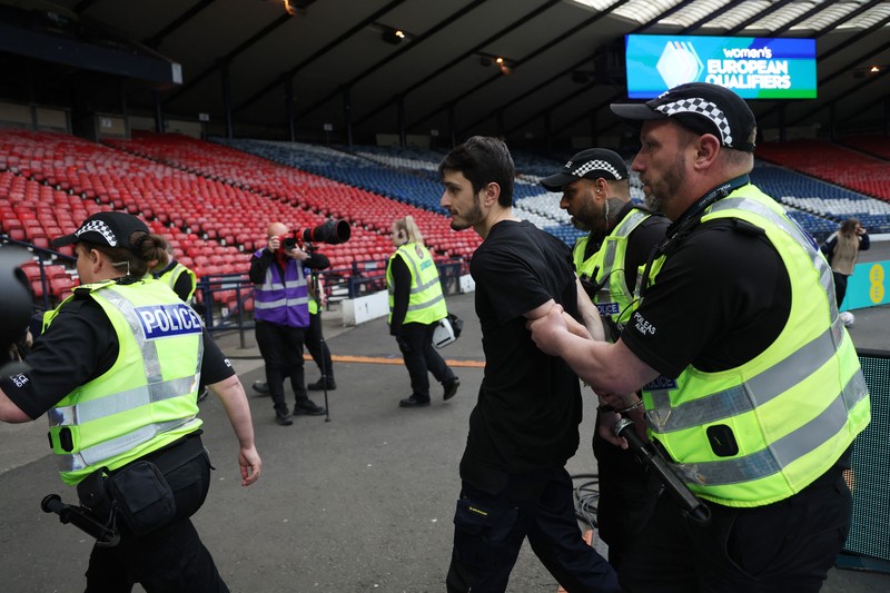 Polisi menahan seorang pengunjuk rasa yang diikat ke tiang gawang di Hampden Park, Glasgow, Skotlandia, Jumat (31/5/2024). (REUTERS/Russell Cheyne) Polisi menahan seorang pengunjuk rasa yang diikat ke tiang gawang di Hampden Park, Glasgow, Skotlandia, Jumat (31/5/2024). (REUTERS/Russell Cheyne)