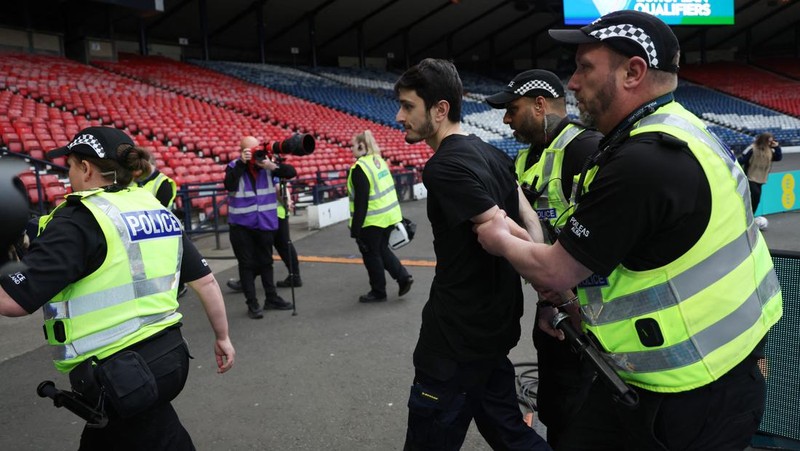 Polisi menahan seorang pengunjuk rasa yang diikat ke tiang gawang di Hampden Park, Glasgow, Skotlandia, Jumat (31/5/2024). (REUTERS/Russell Cheyne)