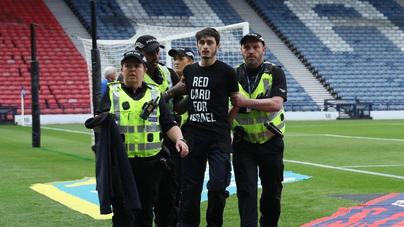 Polisi menahan seorang pengunjuk rasa yang diikat ke tiang gawang di Hampden Park, Glasgow, Skotlandia, Jumat (31/5/2024). (REUTERS/Russell Cheyne)