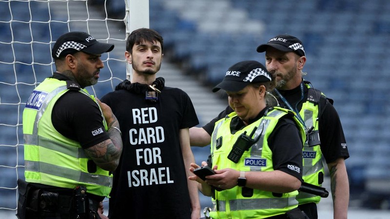 Polisi menahan seorang pengunjuk rasa yang diikat ke tiang gawang di Hampden Park, Glasgow, Skotlandia, Jumat (31/5/2024). (REUTERS/Russell Cheyne)