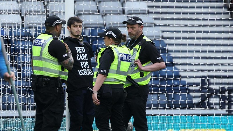 Polisi menahan seorang pengunjuk rasa yang diikat ke tiang gawang di Hampden Park, Glasgow, Skotlandia, Jumat (31/5/2024). (REUTERS/Russell Cheyne)
