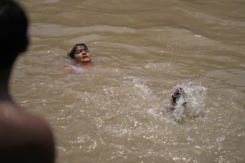 Seorang pria menggendong seorang anak dengan kepala ditutupi handuk untuk melindunginya dari panas di Jammu, India, Minggu, 2 Juni 2024. (AP Photo/Channi Anand)