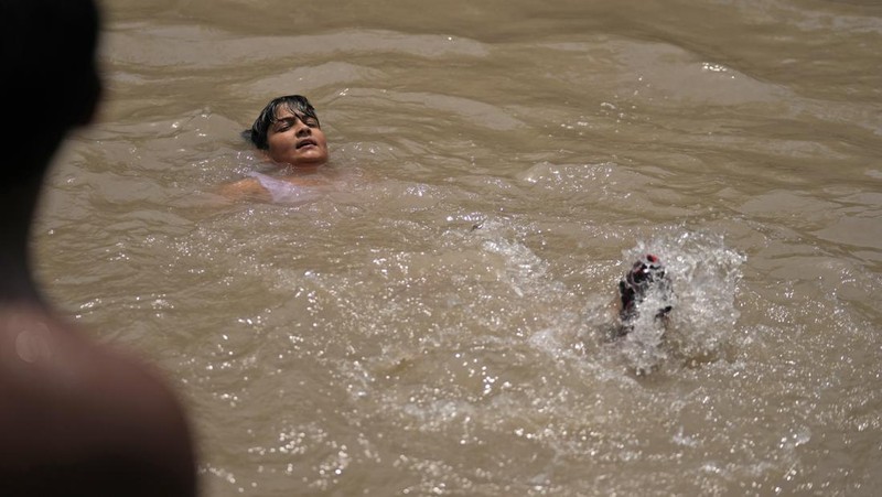 Seorang pria menggendong seorang anak dengan kepala ditutupi handuk untuk melindunginya dari panas di Jammu, India, Minggu, 2 Juni 2024. (AP Photo/Channi Anand)