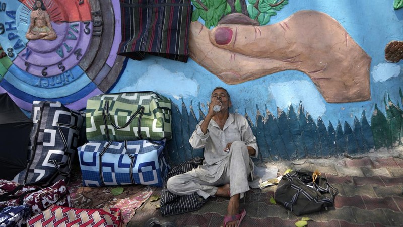 Seorang pria menggendong seorang anak dengan kepala ditutupi handuk untuk melindunginya dari panas di Jammu, India, Minggu, 2 Juni 2024. (AP Photo/Channi Anand)