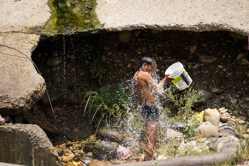 Seorang pria menggendong seorang anak dengan kepala ditutupi handuk untuk melindunginya dari panas di Jammu, India, Minggu, 2 Juni 2024. (AP Photo/Channi Anand)