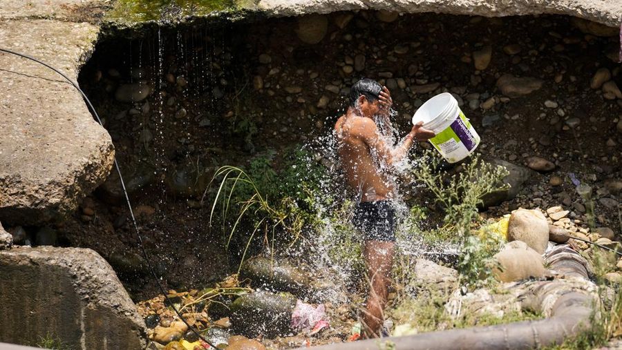 Seorang pria mendinginkan diri dengan mandi menggunakan air yang diambil dari pipa kota yang bocor pada hari musim panas di pinggiran Jammu, India, Jumat, 31 Mei 2024. Para pejabat mengatakan gelombang panas yang menyengat telah menewaskan sedikitnya 14 orang, termasuk 10 petugas pemilu, di India timur dengan suhu melonjak hingga 49,9 derajat Celcius (122 derajat Fahrenheit) di beberapa bagian India minggu ini. (AP Photo/Channi Anand)