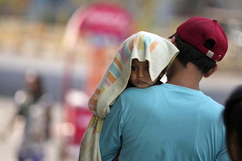 Seorang pria menggendong seorang anak dengan kepala ditutupi handuk untuk melindunginya dari panas di Jammu, India, Minggu, 2 Juni 2024. Seorang pria menggendong seorang anak dengan kepala ditutupi handuk untuk melindunginya dari panas di Jammu, India, Minggu, 2 Juni 2024. (AP Photo/Channi Anand)