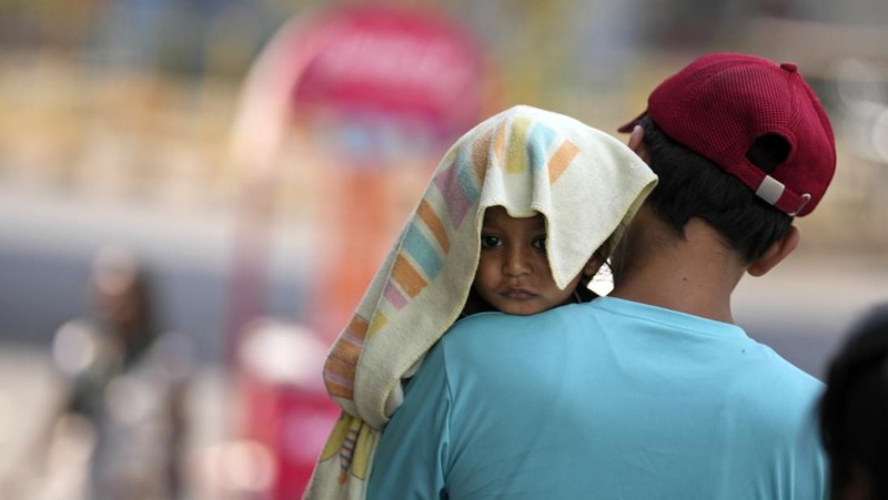 Seorang pria menggendong seorang anak dengan kepala ditutupi handuk untuk melindunginya dari panas di Jammu, India, Minggu, 2 Juni 2024. (AP Photo/Channi Anand)