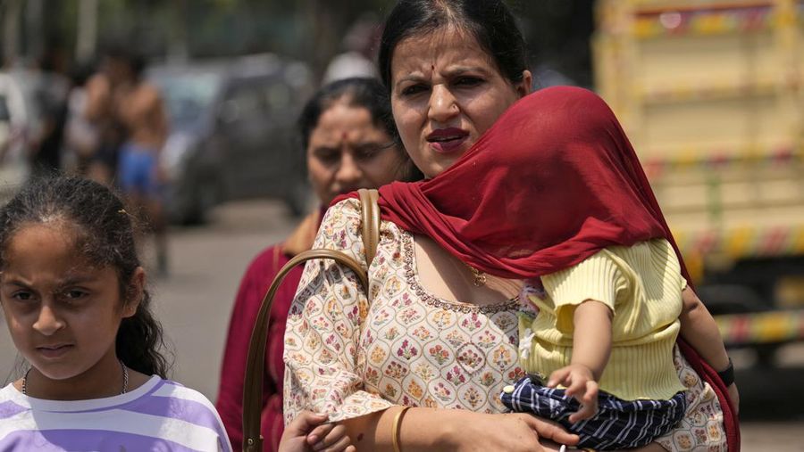 Seorang pria menggendong seorang anak dengan kepala ditutupi handuk untuk melindunginya dari panas di Jammu, India, Minggu, 2 Juni 2024. (AP Photo/Channi Anand)