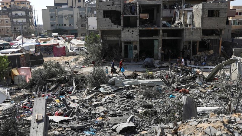 Orang-orang berjalan di antara puing-puing, setelah serangan Israel di daerah tersebut, di mana sandera Israel diselamatkan pada hari Sabtu, ketika jumlah korban tewas warga Palestina meningkat menjadi 274, di tengah konflik Israel-Hamas, di kamp pengungsi Nuseirat di Jalur Gaza tengah, 9 Juni 2024 . (REUTERS/Abed Khaled)