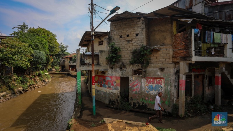 Seorang warga berjalan di dekat rumah yang rusak akibat sering terendam banjir di kawasan Cililitan, Jakarta, Selasa (11/6/2024). Seorang warga berjalan di dekat rumah yang rusak akibat sering terendam banjir di kawasan Cililitan, Jakarta, Selasa (11/6/2024). (CNBC Indonesia/Faisal Rahman)