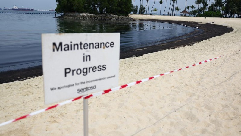 Seorang pria duduk di dekat papan tanda dan pita penjagaan dipasang menyusul tumpahan minyak di Pantai Tanjong di Sentosa, Singapura 15 Juni 2024. (REUTERS/Edgar Su)