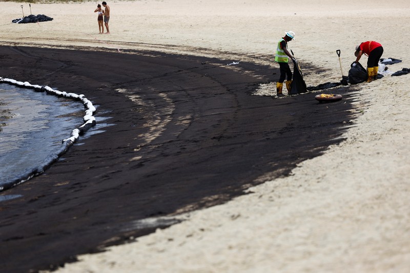 Seorang pria duduk di dekat papan tanda dan pita penjagaan dipasang menyusul tumpahan minyak di Pantai Tanjong di Sentosa, Singapura 15 Juni 2024. (REUTERS/Edgar Su)