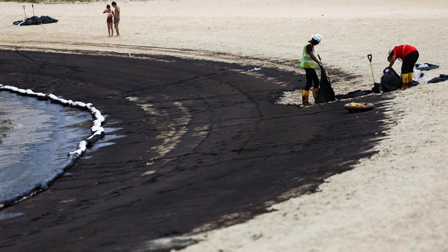Seorang pria duduk di dekat papan tanda dan pita penjagaan dipasang menyusul tumpahan minyak di Pantai Tanjong di Sentosa, Singapura 15 Juni 2024. (REUTERS/Edgar Su)