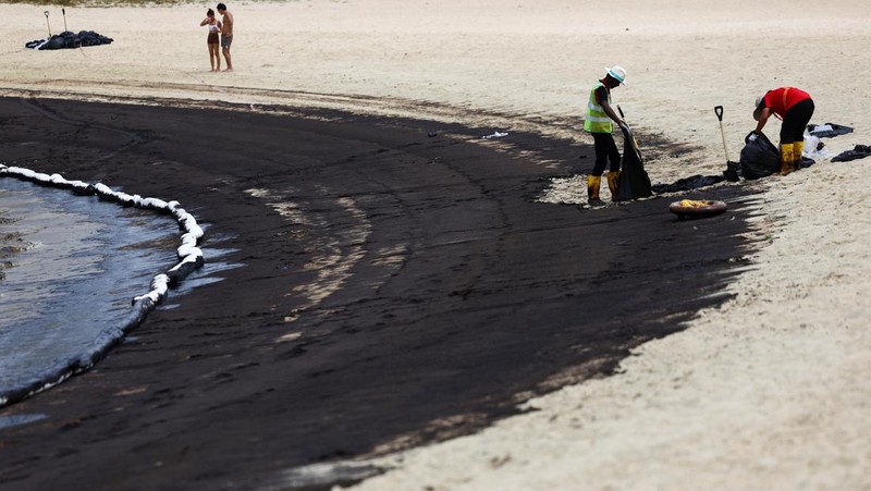 Seorang pria duduk di dekat papan tanda dan pita penjagaan dipasang menyusul tumpahan minyak di Pantai Tanjong di Sentosa, Singapura 15 Juni 2024. (REUTERS/Edgar Su)