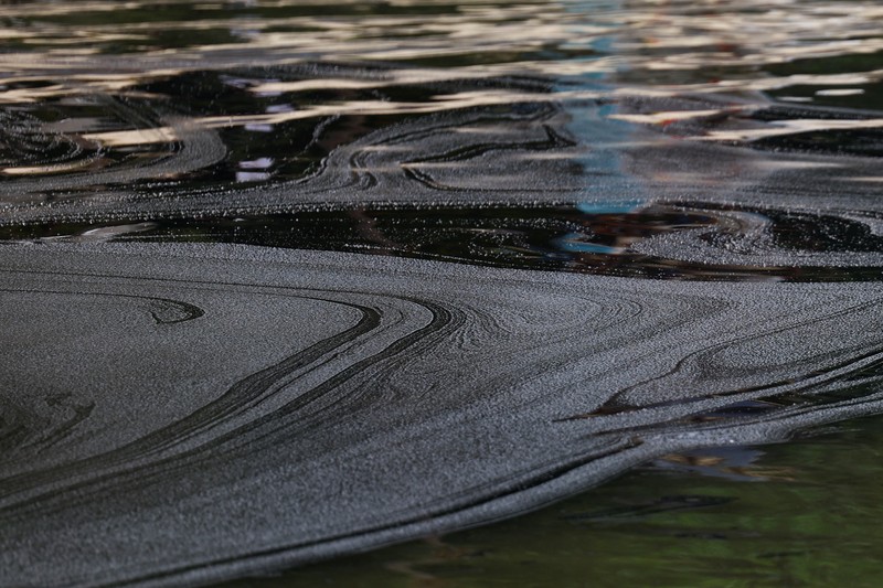 Seorang pria duduk di dekat papan tanda dan pita penjagaan dipasang menyusul tumpahan minyak di Pantai Tanjong di Sentosa, Singapura 15 Juni 2024. (REUTERS/Edgar Su)