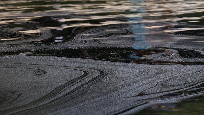 Seorang pria duduk di dekat papan tanda dan pita penjagaan dipasang menyusul tumpahan minyak di Pantai Tanjong di Sentosa, Singapura 15 Juni 2024. (REUTERS/Edgar Su)