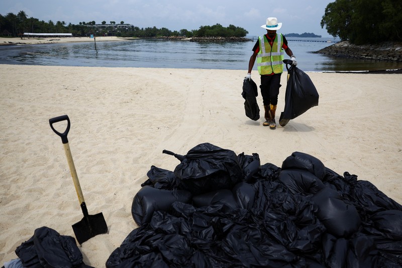 Seorang pria duduk di dekat papan tanda dan pita penjagaan dipasang menyusul tumpahan minyak di Pantai Tanjong di Sentosa, Singapura 15 Juni 2024. Seorang pria duduk di dekat papan tanda dan pita penjagaan dipasang menyusul tumpahan minyak di Pantai Tanjong di Sentosa, Singapura 15 Juni 2024. (REUTERS/Edgar Su)