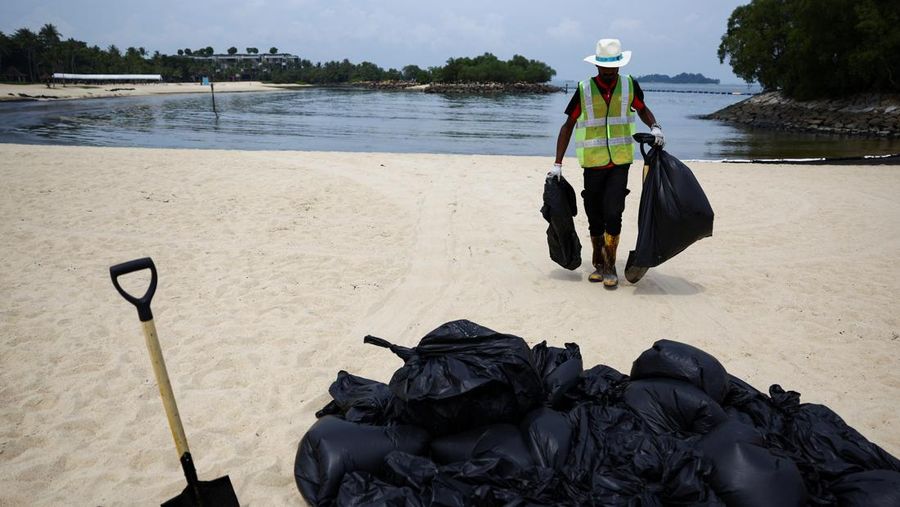 Seorang pria duduk di dekat papan tanda dan pita penjagaan dipasang menyusul tumpahan minyak di Pantai Tanjong di Sentosa, Singapura 15 Juni 2024. (REUTERS/Edgar Su)