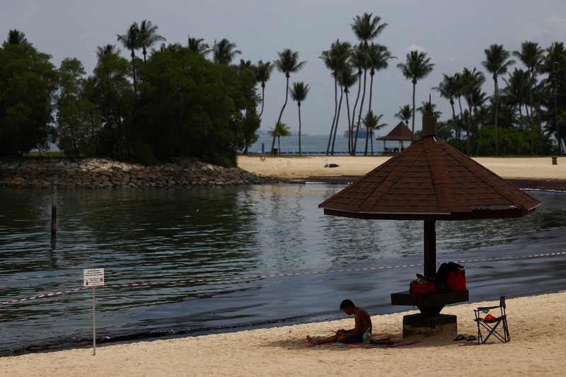 Seorang pria duduk di dekat papan tanda dan pita penjagaan dipasang menyusul tumpahan minyak di Pantai Tanjong di Sentosa, Singapura 15 Juni 2024. Seorang pria duduk di dekat papan tanda dan pita penjagaan dipasang menyusul tumpahan minyak di Pantai Tanjong di Sentosa, Singapura 15 Juni 2024. (REUTERS/Edgar Su)