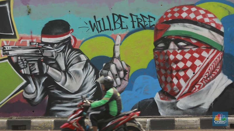 Pengendara sepeda motor melintasi mural dengan gambar wajah PM Israel, Benjamin Netanyahu dengan tulisan Stop Genocide di Kawasan Sudirman, Tanah Abang, Jakarta Pusat, Rabu (19/6/2024). (CNBC Indonesia/Muhammad Sabki)