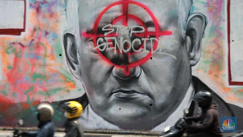 Pengendara sepeda motor melintasi mural dengan gambar wajah PM Israel, Benjamin Netanyahu dengan tulisan Stop Genocide di Kawasan Sudirman, Tanah Abang, Jakarta Pusat, Rabu (19/6/2024). (CNBC Indonesia/Muhammad Sabki)