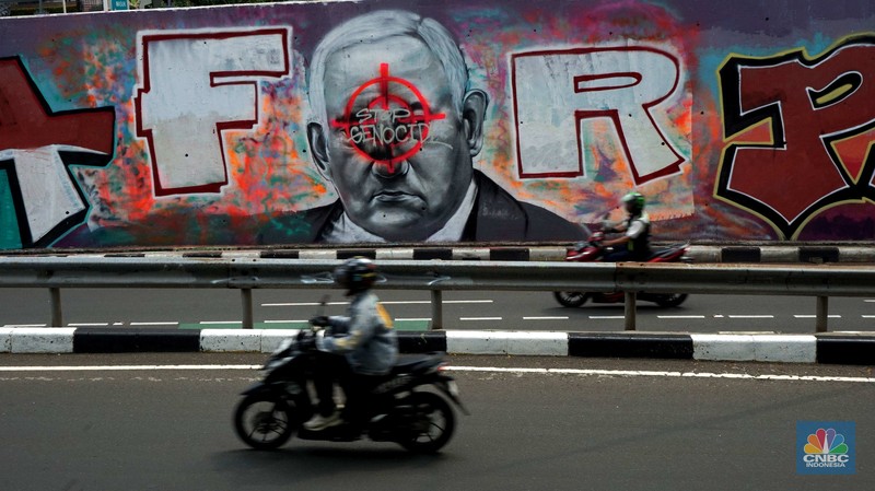 Pengendara sepeda motor melintasi mural dengan gambar wajah PM Israel, Benjamin Netanyahu dengan tulisan Stop Genocide di Kawasan Sudirman, Tanah Abang, Jakarta Pusat, Rabu (19/6/2024). Pengendara sepeda motor melintasi mural dengan gambar wajah PM Israel, Benjamin Netanyahu dengan tulisan Stop Genocide di Kawasan Sudirman, Tanah Abang, Jakarta Pusat, Rabu (19/6/2024). (CNBC Indonesia/Muhammad Sabki)