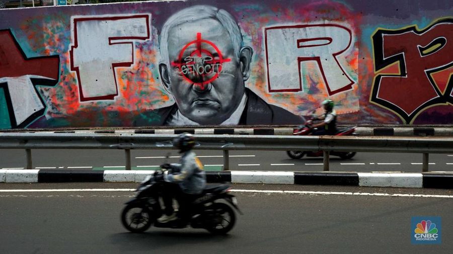 Pengendara sepeda motor melintasi mural dengan gambar wajah PM Israel, Benjamin Netanyahu dengan tulisan Stop Genocide di Kawasan Sudirman, Tanah Abang, Jakarta Pusat, Rabu (19/6/2024). (CNBC Indonesia/Muhammad Sabki)