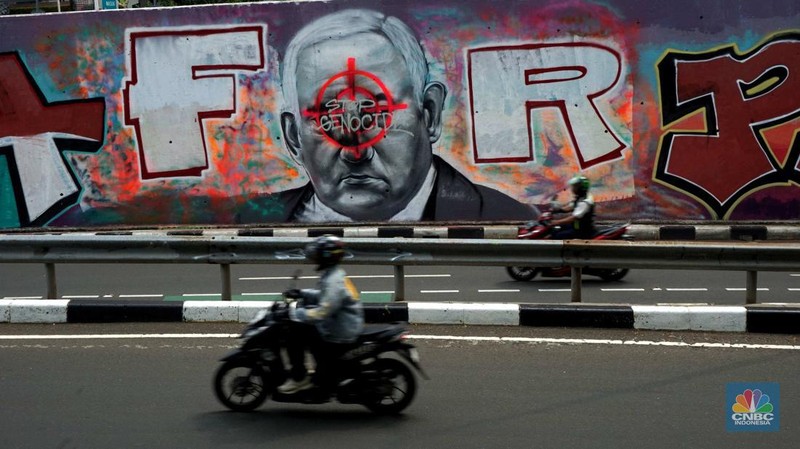 Pengendara sepeda motor melintasi mural dengan gambar wajah PM Israel, Benjamin Netanyahu dengan tulisan Stop Genocide di Kawasan Sudirman, Tanah Abang, Jakarta Pusat, Rabu (19/6/2024). (CNBC Indonesia/Muhammad Sabki)