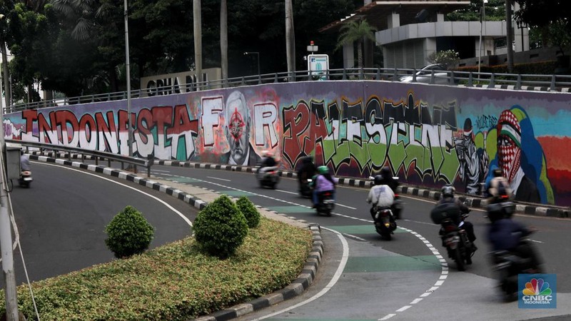 Pengendara sepeda motor melintasi mural dengan gambar wajah PM Israel, Benjamin Netanyahu dengan tulisan Stop Genocide di Kawasan Sudirman, Tanah Abang, Jakarta Pusat, Rabu (19/6/2024). (CNBC Indonesia/Muhammad Sabki)