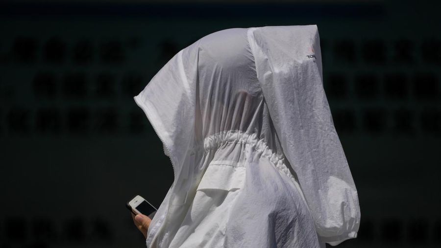Warga Beijing menggunakan pelindung wajah saat beraktivitas diluar rumah di tengah cuaca panas ekstrem. (AP Photo/Andy Wong)