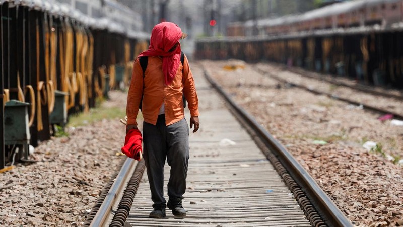 Seorang pria menutupi wajahnya menggunakan kain untuk melindungi dirinya dari sinar matahari saat dia memeriksa rel kereta api pada hari musim panas di New Delhi, India, 18 Juni 2024. (REUTERS/Priyanshu Singh)
