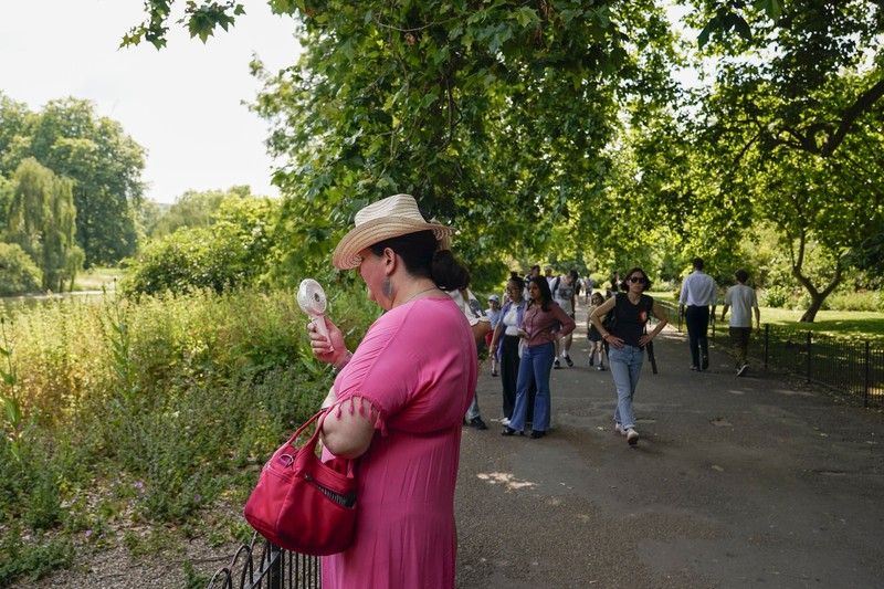 A woman holds a portable fan in St James's park, in London, Tuesday, June 25, 2024, as the temperatures are set to reach 28C during the week. (AP Photo/Alberto Pezzali)