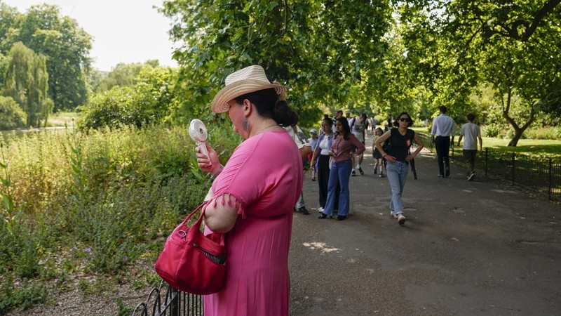 A woman holds a portable fan in St James's park, in London, Tuesday, June 25, 2024, as the temperatures are set to reach 28C during the week. (AP Photo/Alberto Pezzali)