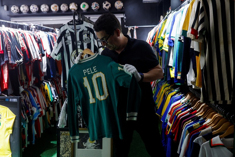 Cassio Brandao, 41, holds a shirt worn by Pele during a match with the presence of Britain's Queen Elizabeth in 1968, in a room filled with clothes racks that in April 2024 made him become a Guinness World Records title holder, as the owner of the world's largest collection of soccer shirts, in Sao Paulo, Brazil June 24, 2024. REUTERS/Amanda Perobelli