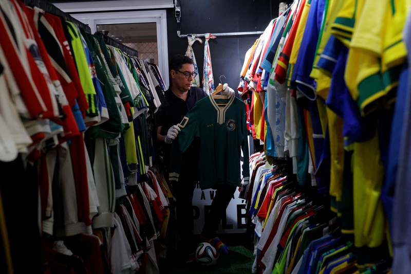 Cassio Brandao, 41, holds a shirt worn by Pele during a match with the presence of Britain's Queen Elizabeth in 1968, in a room filled with clothes racks that in April 2024 made him become a Guinness World Records title holder, as the owner of the world's largest collection of soccer shirts, in Sao Paulo, Brazil June 24, 2024. REUTERS/Amanda Perobelli
