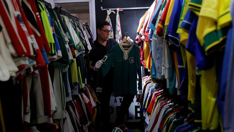 Cassio Brandao, 41, holds a shirt worn by Pele during a match with the presence of Britain's Queen Elizabeth in 1968, in a room filled with clothes racks that in April 2024 made him become a Guinness World Records title holder, as the owner of the world's largest collection of soccer shirts, in Sao Paulo, Brazil June 24, 2024. REUTERS/Amanda Perobelli