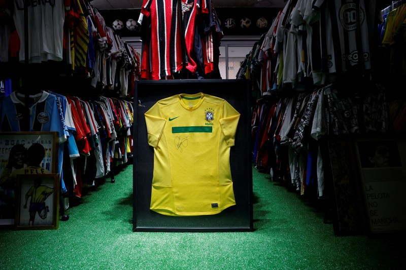 SOCCER-COPA/JERSEY Cassio Brandao, 41, holds a shirt worn by Pele during a match with the presence of Britain's Queen Elizabeth in 1968, in a room filled with clothes racks that in April 2024 made him become a Guinness World Records title holder, as the owner of the world's largest collection of soccer shirts, in Sao Paulo, Brazil June 24, 2024. REUTERS/Amanda Perobelli