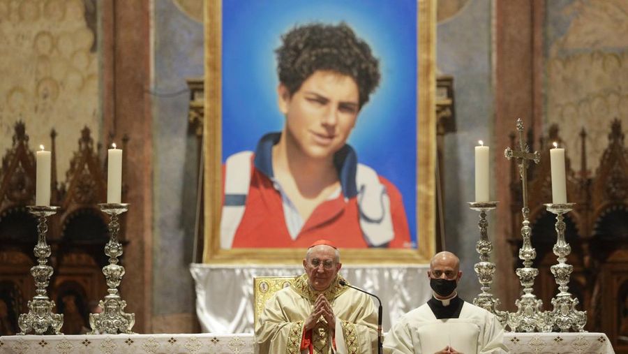 Gambar Carlo Acutis yang berusia 15 tahun, seorang anak laki-laki Italia yang meninggal pada tahun 2006 karena leukemia, terlihat dalam upacara beatifikasi yang dirayakan oleh Kardinal Agostino Vallini, tengah, di Basilika Santo Fransiskus, di Assisi, Italia, pada Oktober 2019. (AP Photo/Gregorio Borgia/File Foto)