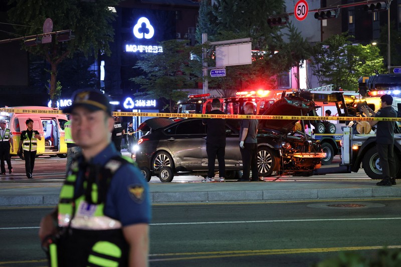 Polisi dan tim penyelamat berdiri di samping mobil yang terlibat dalam kecelakaan yang mengakibatkan beberapa orang tewas dan terluka di pusat kota Seoul, Korea Selatan 1 Juli 2024. (REUTERS/Kim Hong-Ji)