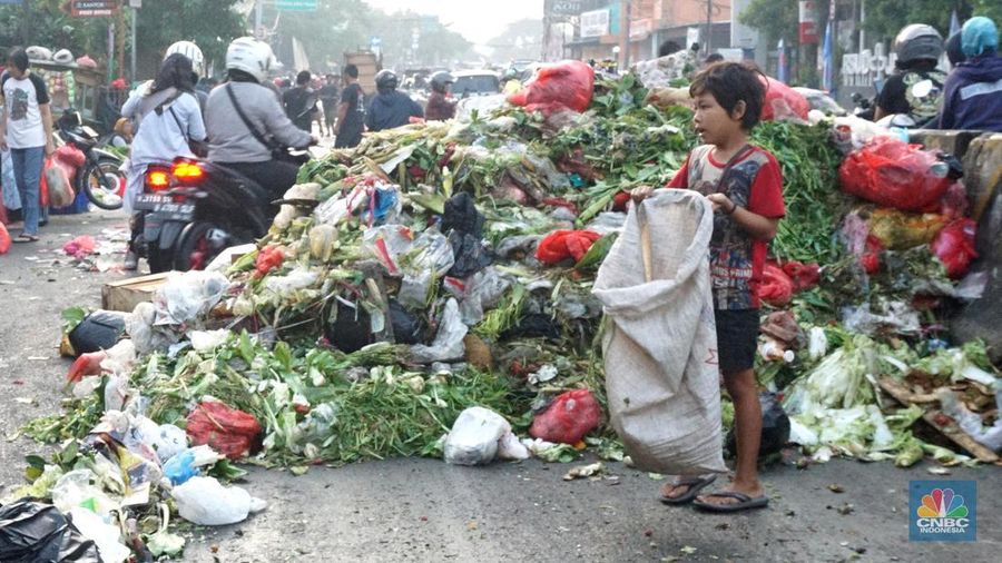 Seorang anak melintas di samping alat berat saat penanganan tumpukan sampah organik dan sisa makanan di kawasan Pasar Minggu, Jakarta, Jumat, (5/7/2024). (CNBC Indonesia/Muhammad Sabki)